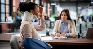 Woman wearing neck brace and arm sling meeting with lawyer at desk