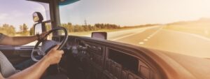 truck driver gripping steering wheel inside cab on open highway