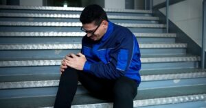 man clutching injured knee while seated on outdoor stairs after fall
