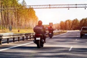two motorcyclists riding highway rear view with forest roadside and overhead gantry