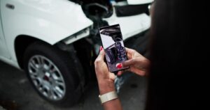 person photographing damaged vehicle with smartphone after car accident